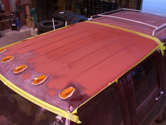Red roof section of a van being prepped for paint, with amber clearance lights and a silver roof rack