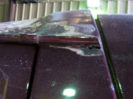 Close-up of rust and body filler on the edge of a dark red vehicle's roof