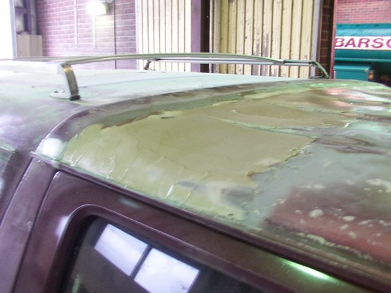 Close-up of a vehicle roof with body filler applied, showing repair work. Roof rack rails are visible