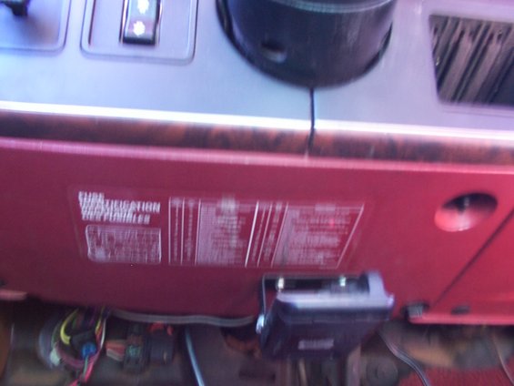Close-up of a red dashboard panel with a white sticker showing vehicle information and wiring below