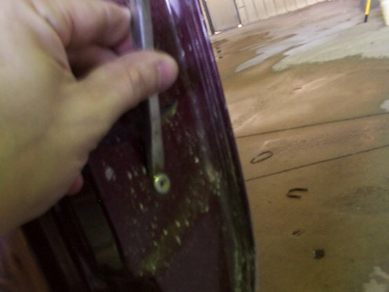 Maroon door panel with a hand holding a metal rod near a screw
