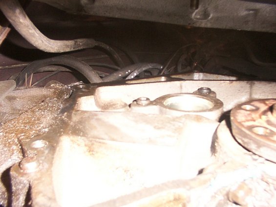 Transmission housing with hoses and bolts. Some fluid residue is visible
