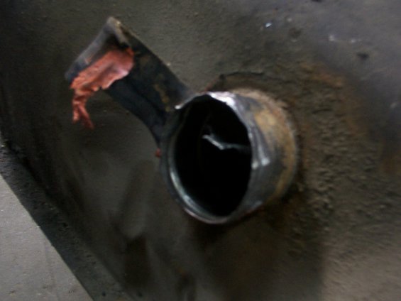 Close-up of a fuel tank filler neck with some red material on the pipe