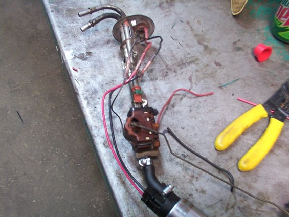 Fuel pump assembly with wires and hoses on a workbench, next to yellow wire cutters