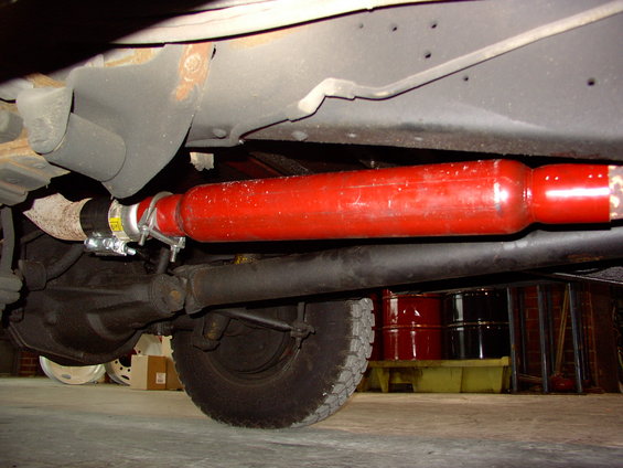 Underside of a vehicle showing a red exhaust pipe, rear axle, and tire. Text visible on clamp