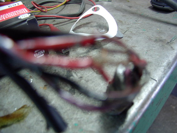 Close-up of a tangled automotive wiring harness with red and black wires, resting on a workbench next to a white plastic part. A NAPA label is visible