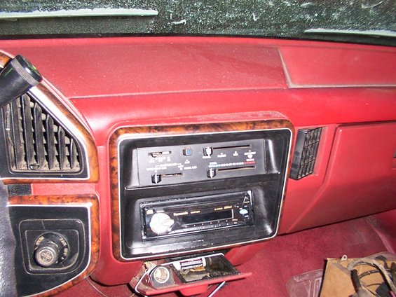Red dashboard interior with wood trim around radio and vents. Open ashtray with cigarette lighter