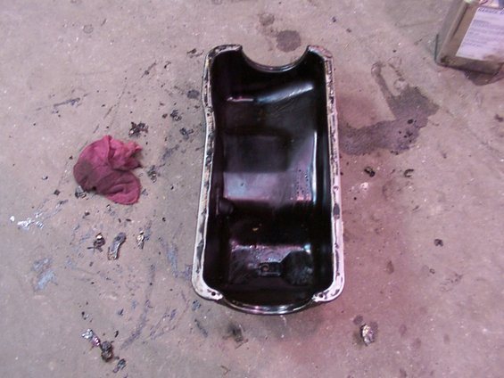 Black oil pan with a red rag and metal debris on a concrete floor