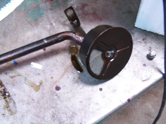 Oil pickup tube with a circular screen and a bent metal pipe, resting on a surface with oil stains
