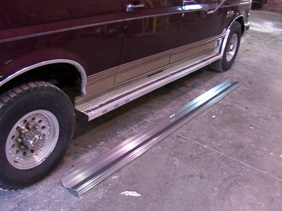 Removed running boards lying on the ground next to a dark red vehicle with tan trim