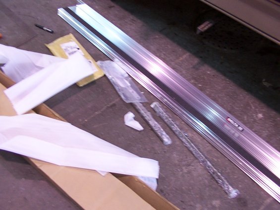 Aluminum running boards with black trim and two metal rods, partially wrapped in plastic