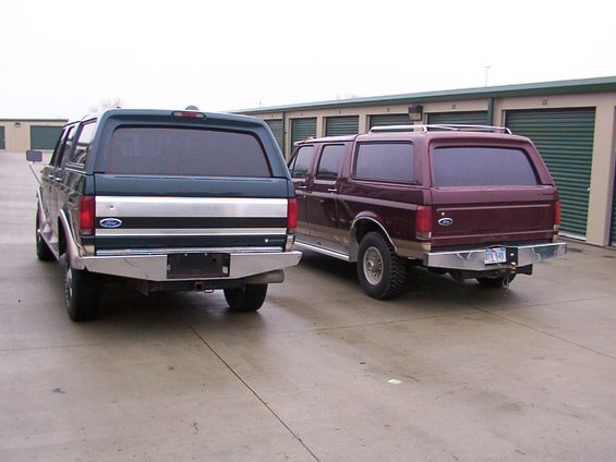 Two Ford Broncos parked outside storage units. One is dark green, the other is maroon