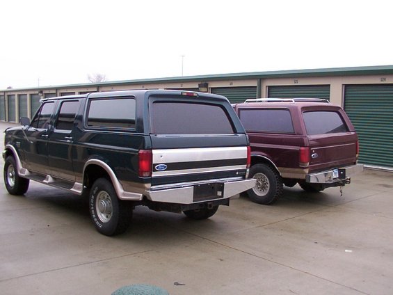 Two Ford Broncos parked side-by-side, rear view. Dark green and maroon
