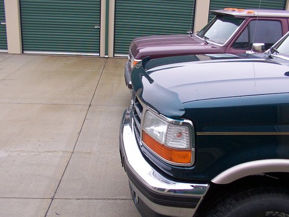 Dark green truck in front of a maroon truck, parked in front of storage unit doors