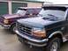 1988 Ford C-350 (Centurion Conversions) - Two Ford F-Series trucks parked in front of storage units, one dark green and one burgundy.