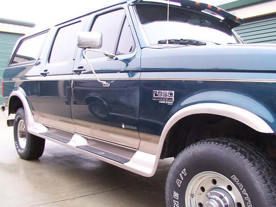 Side view of a dark green Ford F-Series SUV conversion with tan lower trim and running boards. It has a 'F350' badge