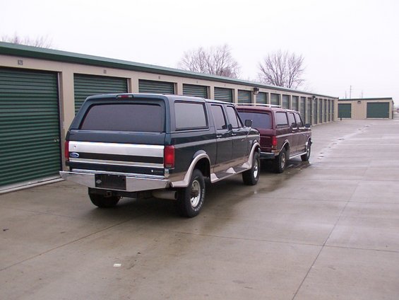 Two Ford Bronco Centurion Conversions parked in front of storage units. The front one is dark green, the rear one is maroon