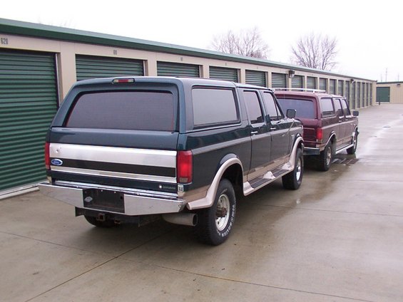 Dark green Ford Bronco Centurion with chrome trim and a silver stripe, parked next to a maroon SUV