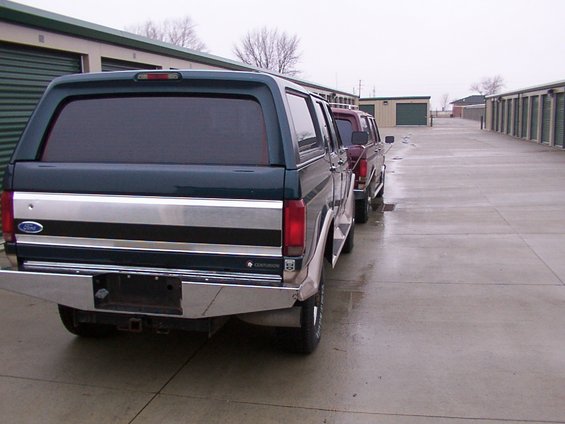Rear view of a dark green and silver 1988 Ford C-350 Centurion Conversions pickup truck with a camper shell, parked in a line