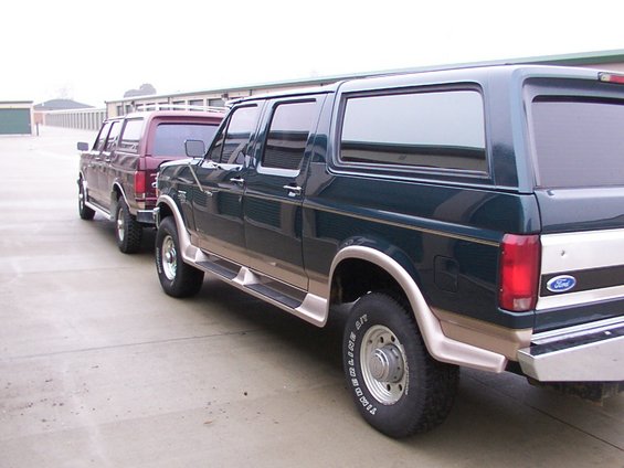Two SUVs parked in front of storage units. The one in front is dark green with tan trim. The one behind it is maroon
