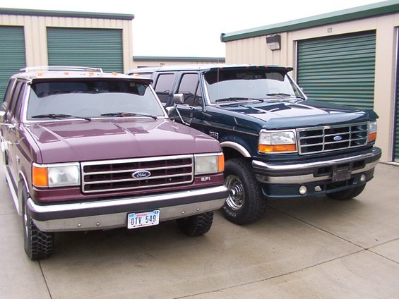 Two Ford trucks, one purple and one dark green, parked in front of storage units