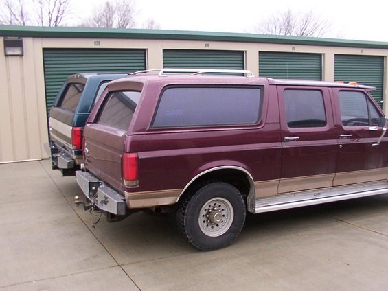 Maroon Ford C-350 Centurion Conversion Van, side view, with a green truck behind it