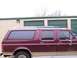 1988 Ford C-350 (Centurion Conversions) - Side view of a maroon van with tan lower body trim and a roof rack parked in front of storage units.
