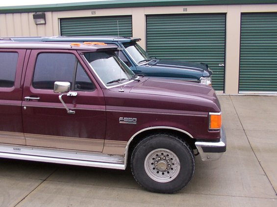 Maroon Ford F-350 extended cab truck parked next to a dark green truck in front of storage units