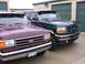 1988 Ford C-350 (Centurion Conversions) - Two Ford trucks are parked side-by-side in front of storage unit doors. The green truck appears to be from the early 1990s.