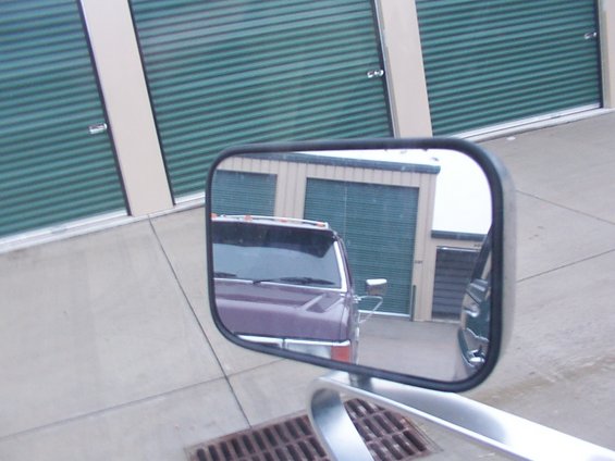 Reflection of a purple pickup truck in a side mirror, parked in front of storage units