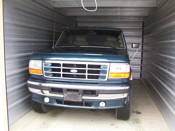 Dark green Ford F-Series truck parked in a storage unit. Front view shows grille and headlights