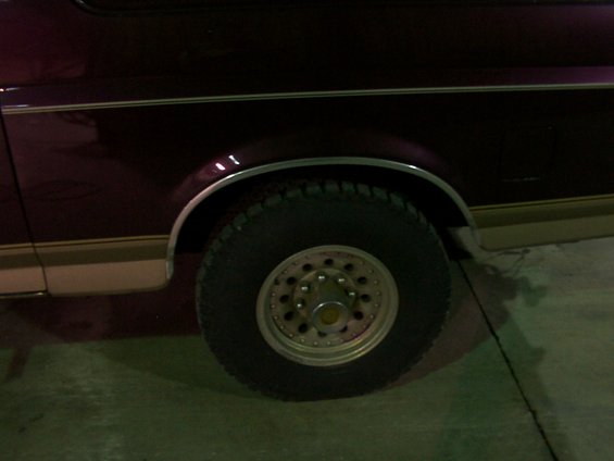 Maroon vehicle side panel with chrome trim above a tan lower body panel, showing a tire and wheel