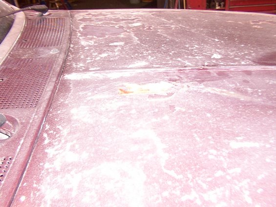 Maroon car hood with faded paint and white residue, showing rust spots and a textured windshield cowl