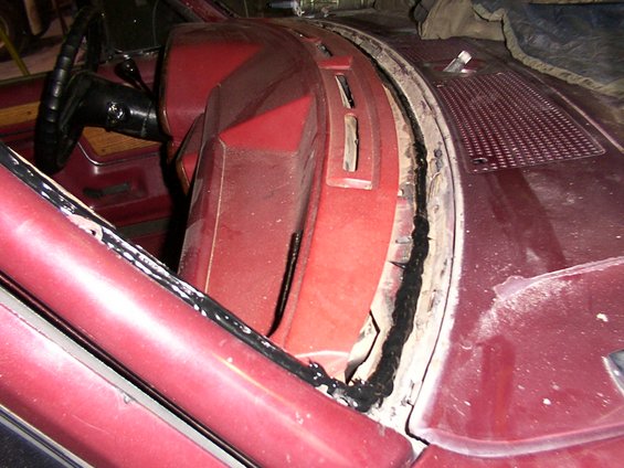 Maroon vehicle interior dashboard with black sealant around windshield frame