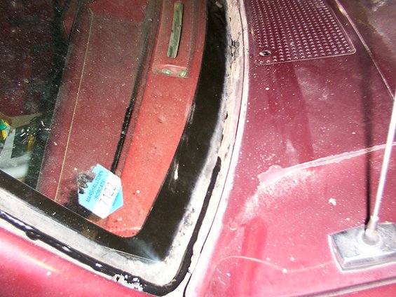 Maroon vehicle windshield frame and hood with rust and a blue sticker