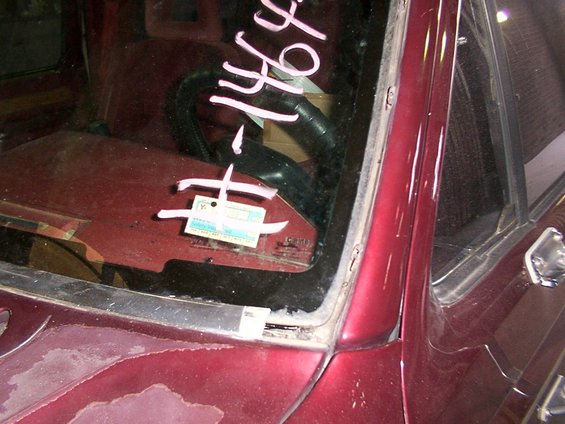 Maroon vehicle interior, showing windshield with pink markings and a small blue and white tag