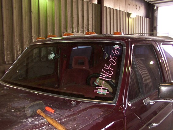 Maroon Ford truck interior with writing on windshield: #1464-05-89. Rubber mallet and screwdriver on hood