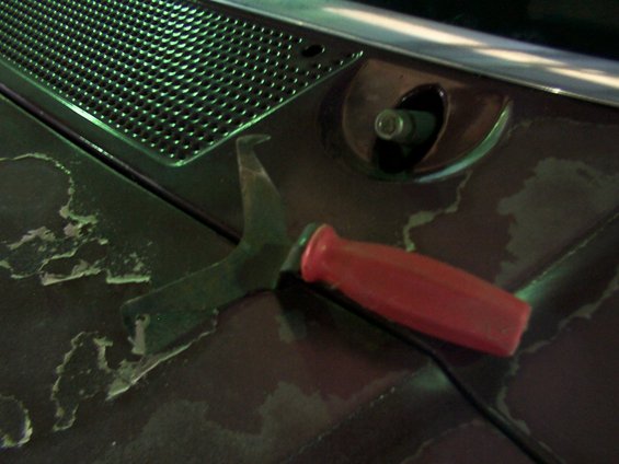 Red-handled tool for removing a windshield wiper arm, resting on a dark surface with peeling paint