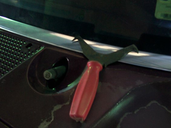 Red-handled trim removal tool on dark brown dashboard near windshield cowl