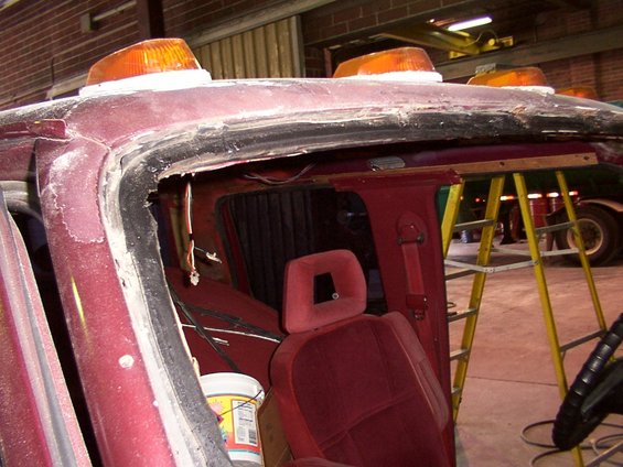 Maroon vehicle interior with red seats, orange roof lights, and a ladder. The windshield area is damaged