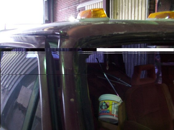 Interior view of a dark-colored vehicle showing a bucket and part of a seat. Amber lights are visible on the roof