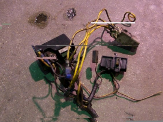 Wiring harness with yellow and black wires, black fuse box, and other electrical connectors on a concrete surface