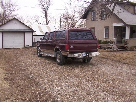 Maroon Ford Bronco SUV with camper shell, rear view, parked in gravel driveway