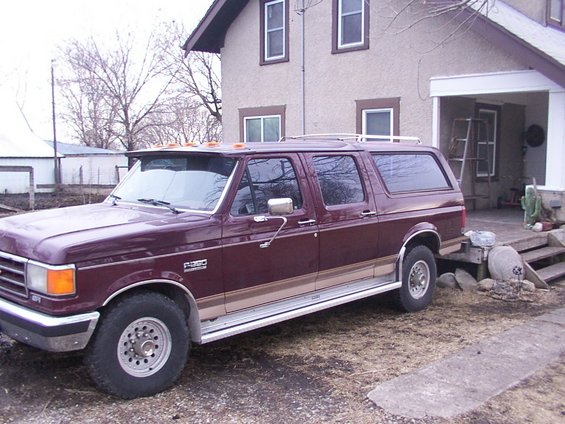 Maroon Ford F-250 extended SUV with tan trim and roof rack parked in front of a house