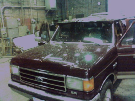 Maroon Ford F-Series truck with open driver door, parked next to a white truck inside a garage