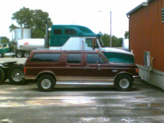 Maroon Ford Bronco Centurion Conversion parked next to a semi-truck