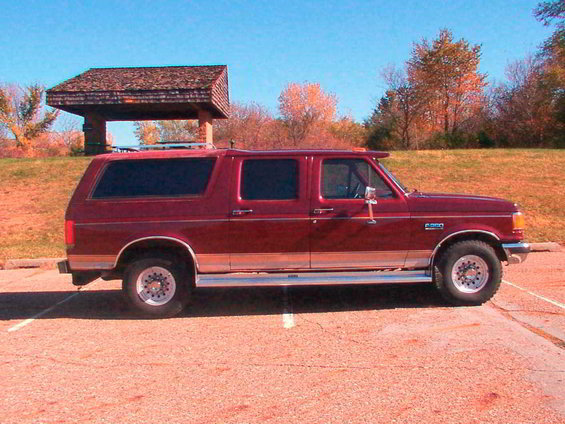 Maroon extended cab SUV parked in a lot, side view. Has a chrome strip along the bottom