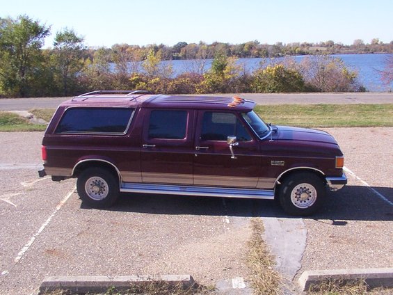 Maroon Ford F-Series SUV conversion with tan trim, parked by a lake