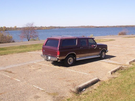 Maroon extended cab pickup with camper shell parked by a lake