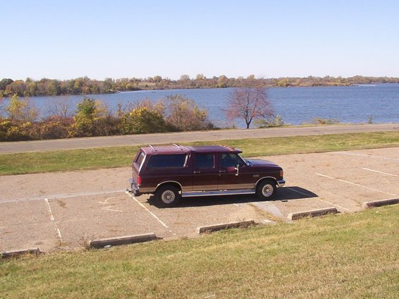 Maroon SUV with camper shell parked by a lake, side view